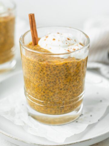 pumpkin spice chia pudding in a glass topped with yogurt and a cinnamon stick.