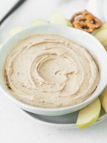 bowl of peanut butter cottage cheese dip on a plate with apple slices and pretzels.