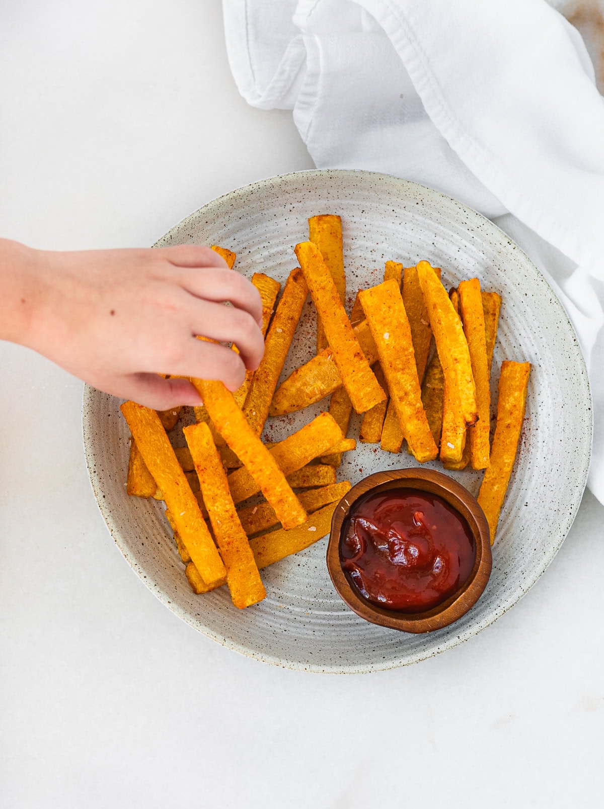 toddler hand reaching for a butternut squash fry from a plate.