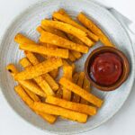 plate of butternut squash fries with a small bowl of ketchup on it.