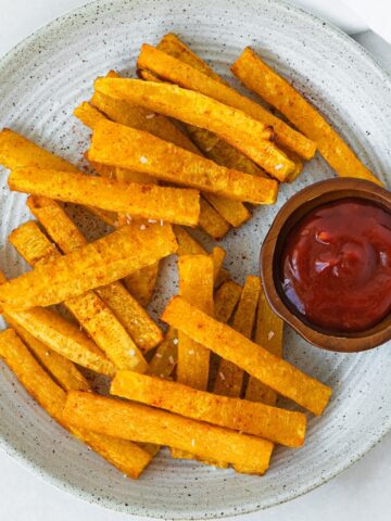 plate of butternut squash fries with a small bowl of ketchup on it.