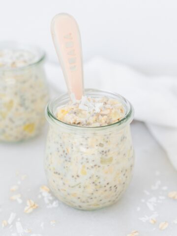 jar of pineapple coconut overnight oats with pink baby spoon in it.