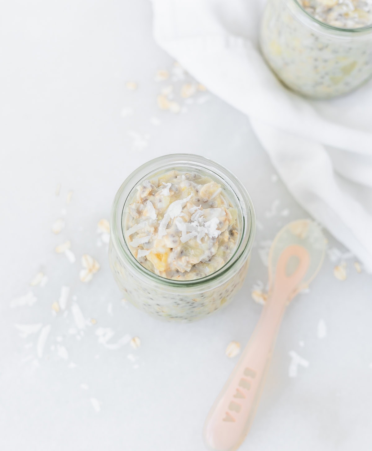 overhead view of a jar of pineapple coconut overnight oats with a pink baby spoon next to it.