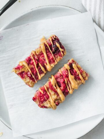 two baby pbj baked oatmeal bars for baby on a small white plate lined with parchment.