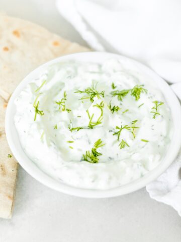 small white bowl of tzatziki sauce with pita wedges and a white napkin.