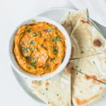 bowl of roasted tomato eggplant dip on a plate with pita wedges.