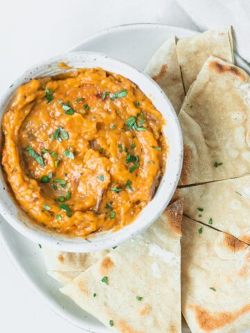 bowl of roasted tomato eggplant dip on a plate with pita wedges.