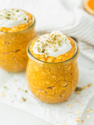 two jars of baby pumpkin spice overnight oats topped with yogurt and pumpkin seeds.